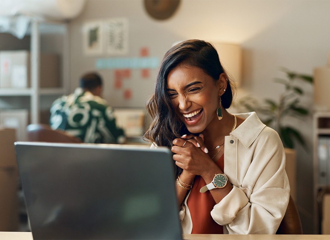 Blog - Excited Woman Holding Hands Together Looking at Laptop Screen in Office